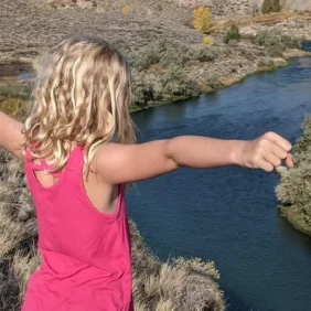 Nathan's daughter standing by cliff overlooking rive with arm out wide