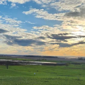 Sunset over American heartland farmland with green fields and dramatic cloudy sky