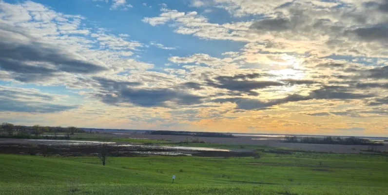 Sunset over American heartland farmland with green fields and dramatic cloudy sky
