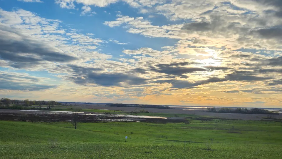 Sunset over American heartland farmland with green fields and dramatic cloudy sky