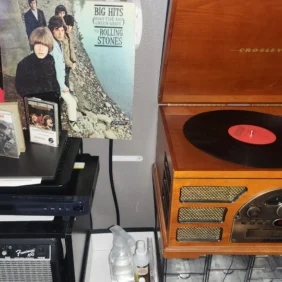 A Crosley record player with The Rolling Stones Big Hits record spinning on the turntable surrounded by CDs and records