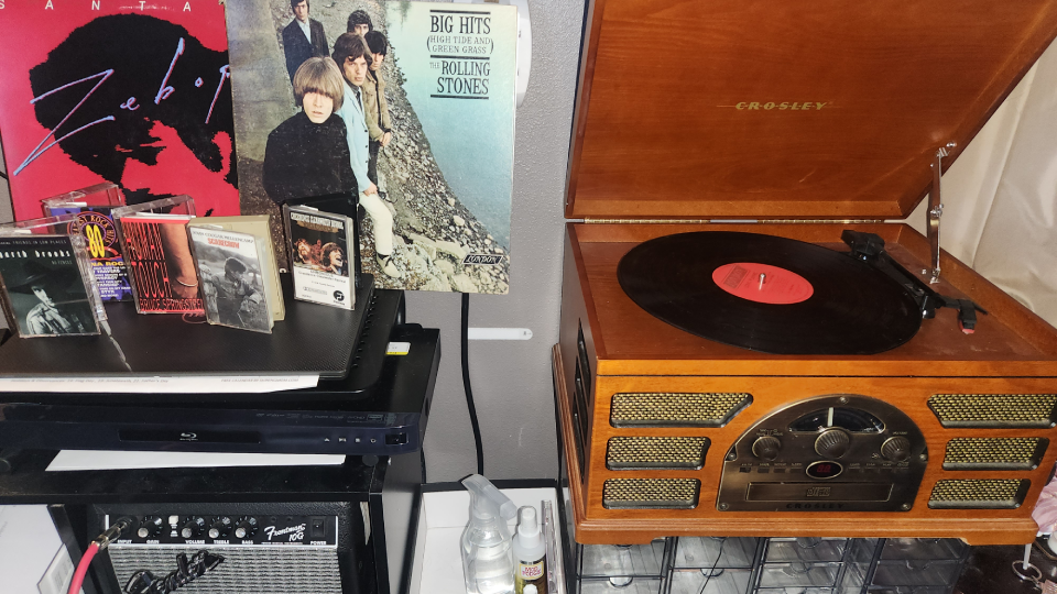 A Crosley record player with The Rolling Stones Big Hits record spinning on the turntable surrounded by CDs and records