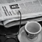 newspaper glasses, and cup of coffee sitting on a table