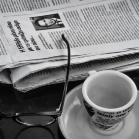 newspaper glasses, and cup of coffee sitting on a table
