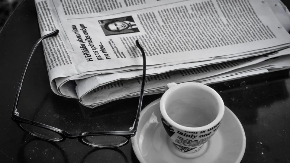 newspaper glasses, and cup of coffee sitting on a table